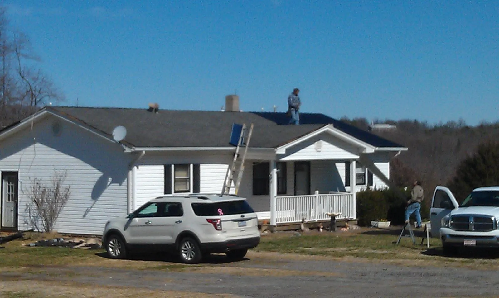 Roofers stripping shingles from a white ranch house roof in Lansford