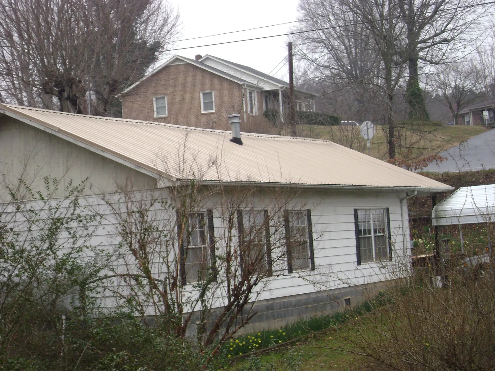 Tan metal roof on a white sided house set into a hillside — Commercial Roofing by Roofing Brothers in Lansford